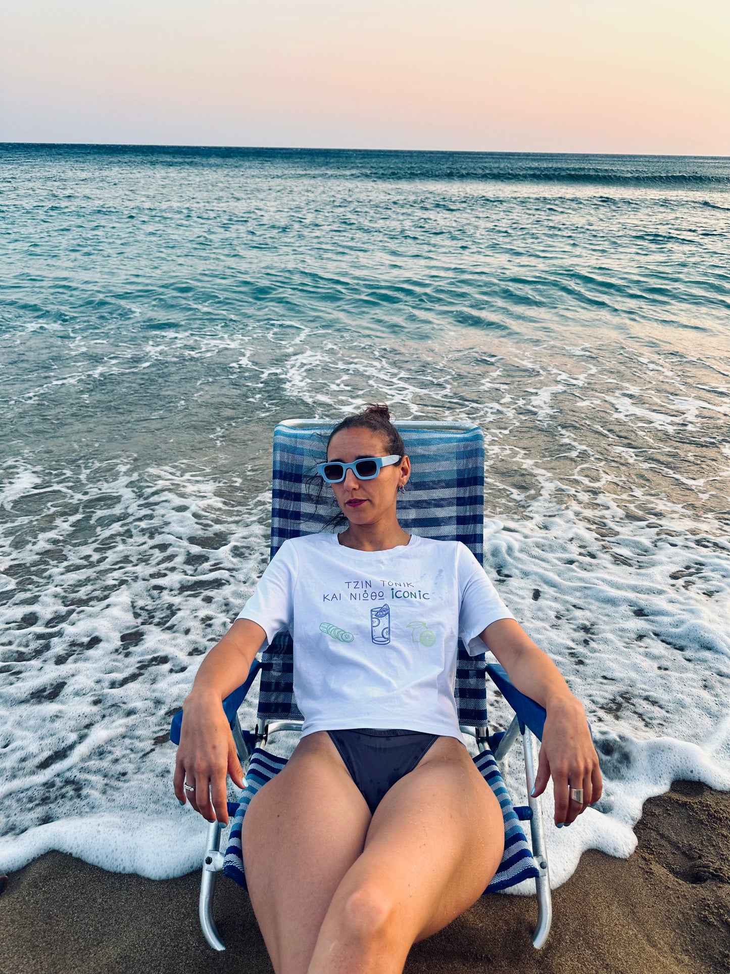 Woman sitting on a beach chair by the ocean with sunglasses on