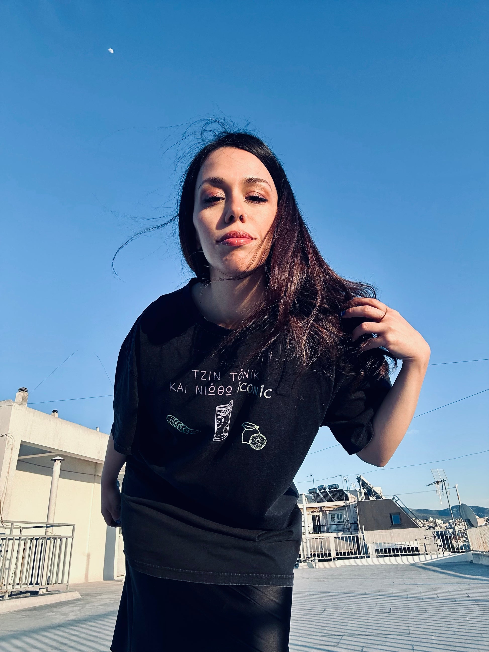 Woman wearing a black t-shirt with text and graphics on a rooftop with a clear blue sky.