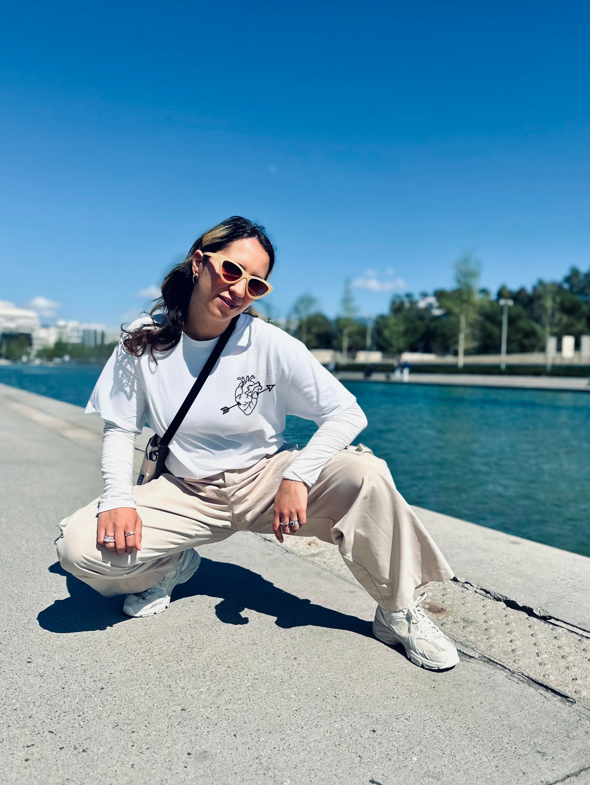 Person sitting on a concrete ledge by a waterfront with a clear blue sky.