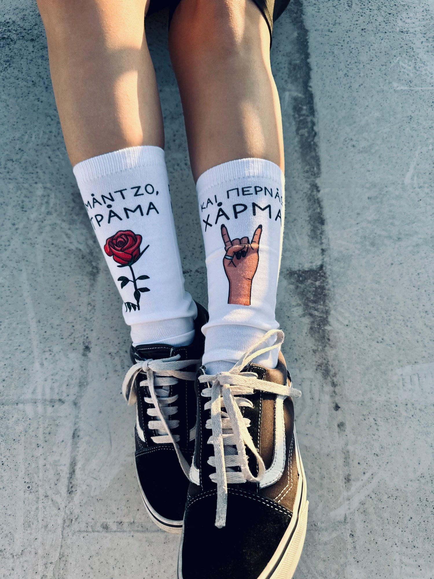 A pair of white crew socks with a graphic design featuring a rose, a hand making a peace sign, and the text 'Romantzo Kampa' displayed on the side.