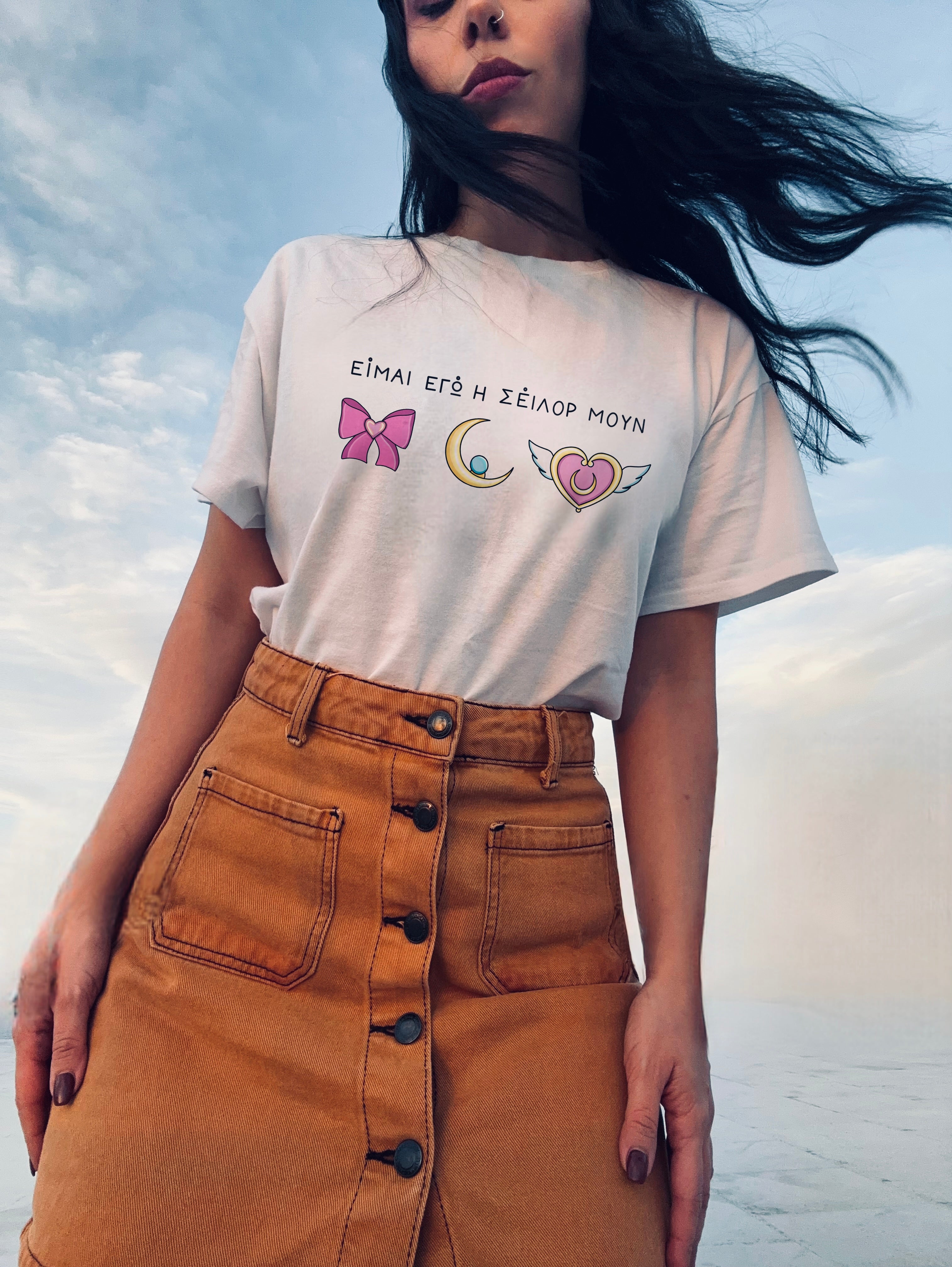Person wearing a white t-shirt with graphics and text, standing against a cloudy sky.